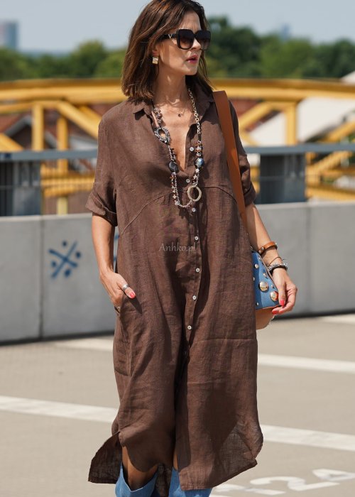 Brązowa lniana sukienka maxi w stylu szmizjerki, zapinana na guziki, o luźnym fasonie oversize, stylizowana z wysokimi kozakami i torebką.