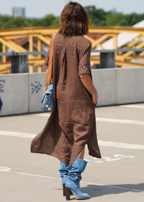 Brązowa lniana sukienka maxi w stylu szmizjerki, zapinana na guziki, o luźnym fasonie oversize, stylizowana z wysokimi kozakami i torebką.