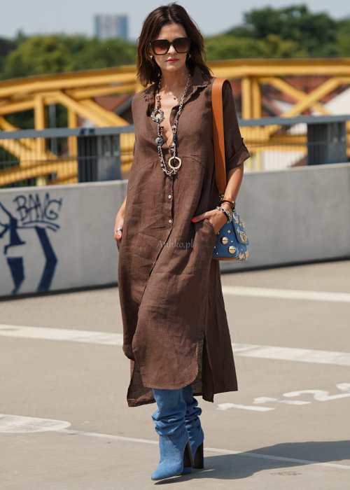 Brązowa lniana sukienka maxi w stylu szmizjerki, zapinana na guziki, o luźnym fasonie oversize, stylizowana z wysokimi kozakami i torebką.