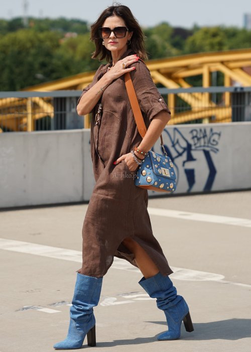Brązowa lniana sukienka maxi w stylu szmizjerki, zapinana na guziki, o luźnym fasonie oversize, stylizowana z wysokimi kozakami i torebką.
