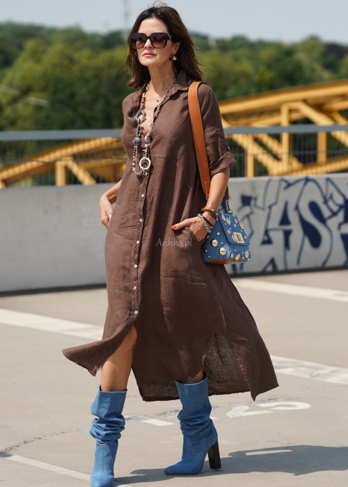 Brązowa lniana sukienka maxi w stylu szmizjerki, zapinana na guziki, o luźnym fasonie oversize, stylizowana z wysokimi kozakami i torebką.