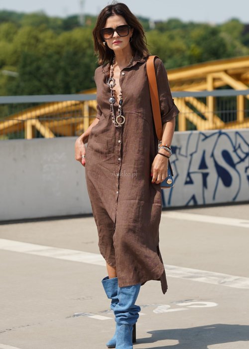 Brązowa lniana sukienka maxi w stylu szmizjerki, zapinana na guziki, o luźnym fasonie oversize, stylizowana z wysokimi kozakami i torebką.