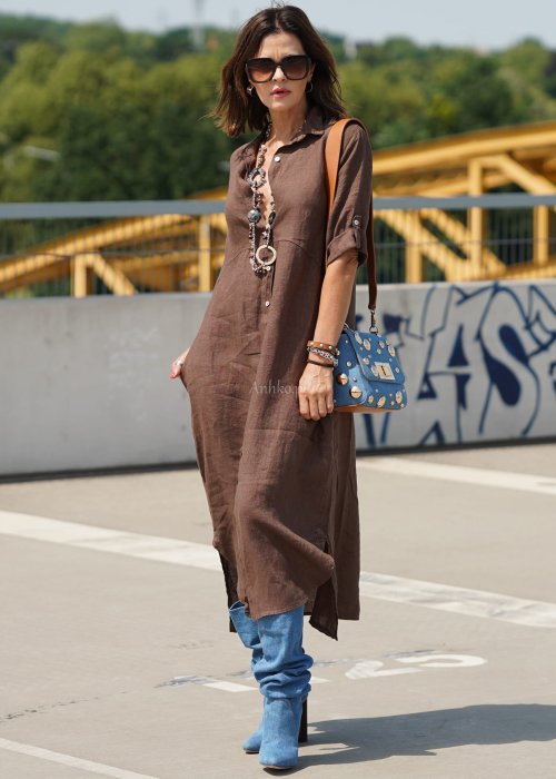 Brązowa lniana sukienka maxi w stylu szmizjerki, zapinana na guziki, o luźnym fasonie oversize, stylizowana z wysokimi kozakami i torebką.