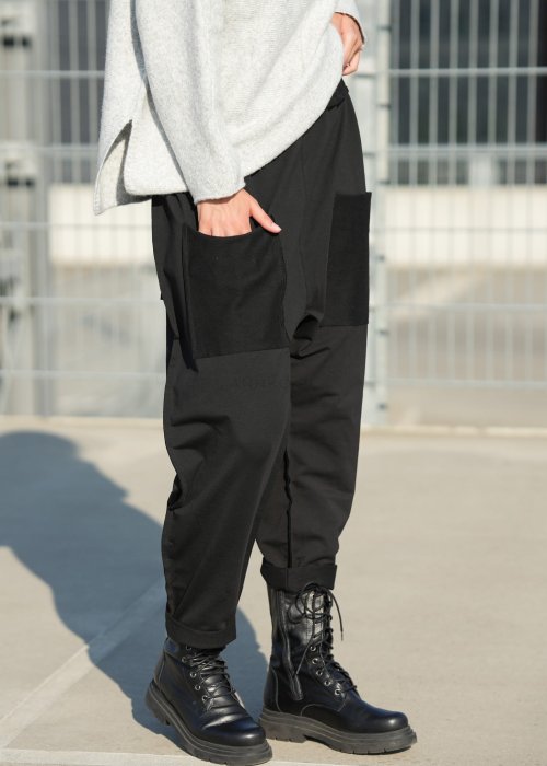 Czarne spodnie damskie o luźnym kroju z dużymi naszywanymi kieszeniami, zestawione z szarym swetrem i czarnymi botkami w miejskiej stylizacji.
