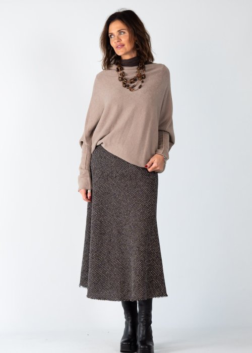Sweter damski oversize w kolorze taupe o kroju nietoperzowym z dekoltem łódka i asymetrycznym dołem, stylizacja z biżuterią.
