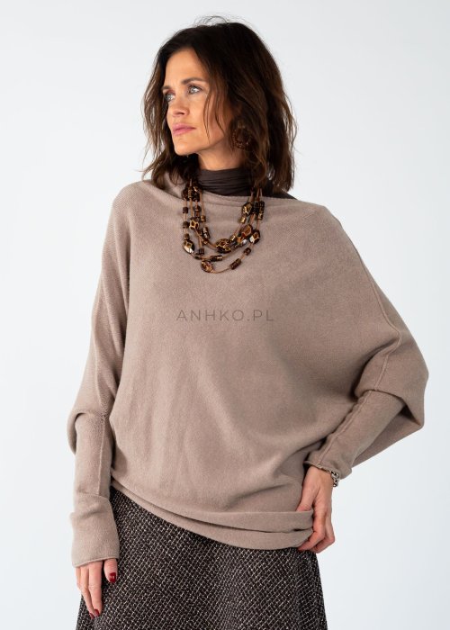 Sweter damski oversize w kolorze taupe o kroju nietoperzowym z dekoltem łódka i asymetrycznym dołem, stylizacja z biżuterią.
