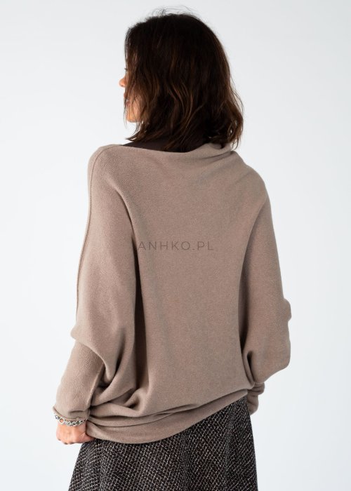 Sweter damski oversize w kolorze taupe o kroju nietoperzowym z dekoltem łódka i asymetrycznym dołem, stylizacja z biżuterią.