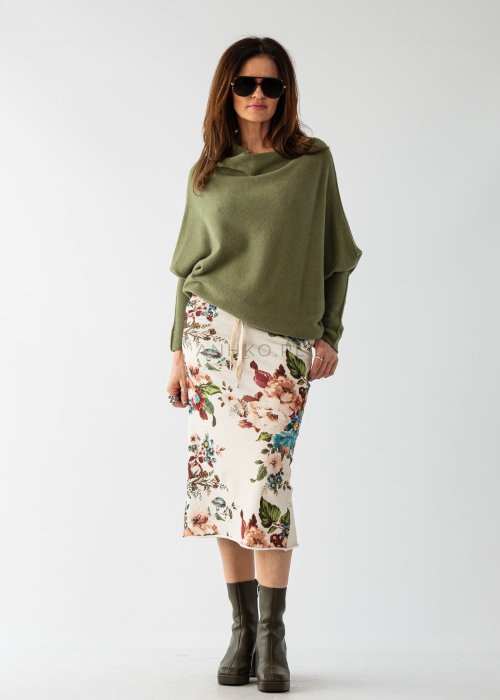Oliwkowy sweter damski oversize o nietoperzowym kroju z dekoltem łódka, luźna stylizacja z wzorzystą spódnicą.