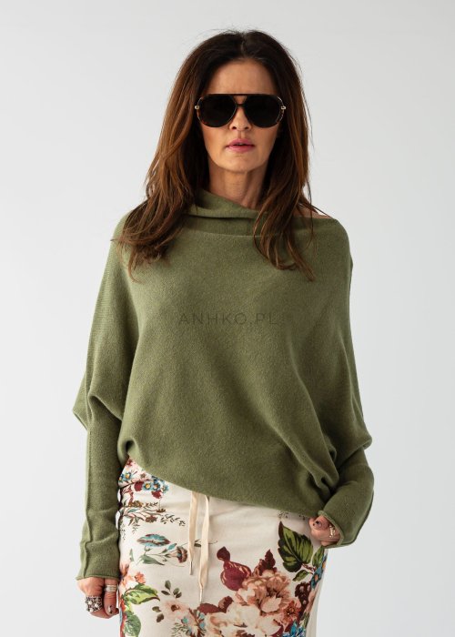 Oliwkowy sweter damski oversize o nietoperzowym kroju z dekoltem łódka, luźna stylizacja z wzorzystą spódnicą.