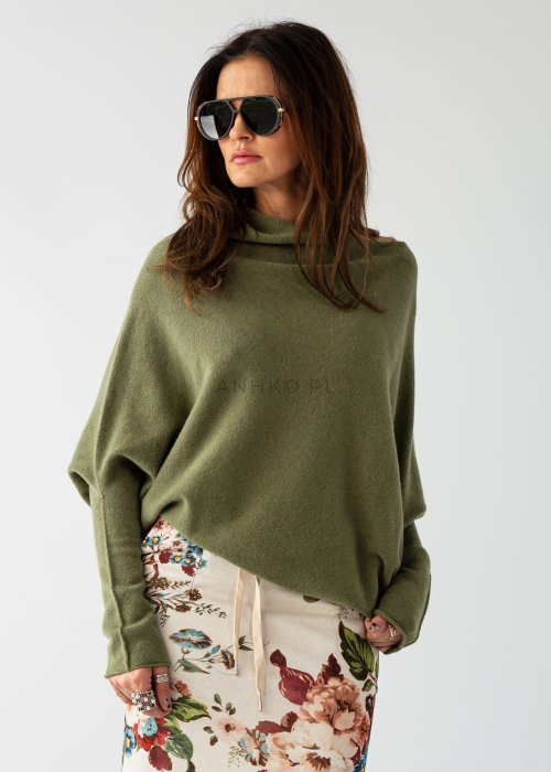 Oliwkowy sweter damski oversize o nietoperzowym kroju z dekoltem łódka, luźna stylizacja z wzorzystą spódnicą.