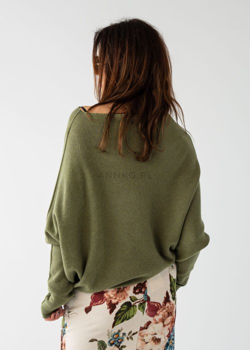 Oliwkowy sweter damski oversize o nietoperzowym kroju z dekoltem łódka, luźna stylizacja z wzorzystą spódnicą.