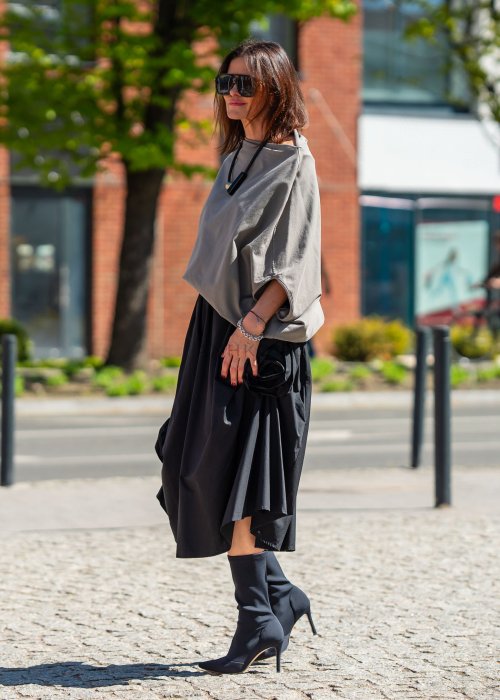 Bluzka damska taupe oversize z rękawami typu nietoperz i opadającym dekoltem, zestawiona z czarną spódnicą. Minimalistyczna stylizacja miejska.
