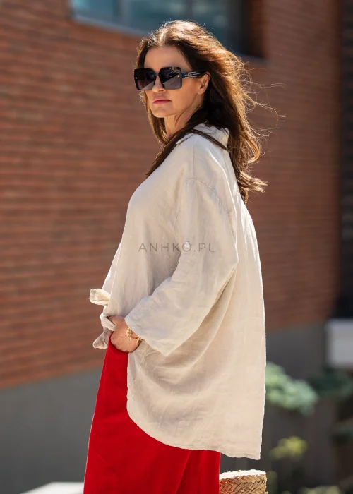 Beżowa lniana koszula damska oversize z asymetrycznym dołem i podpinanymi rękawami, zestawiona z czerwonymi spodniami w eleganckiej stylizacji casual.