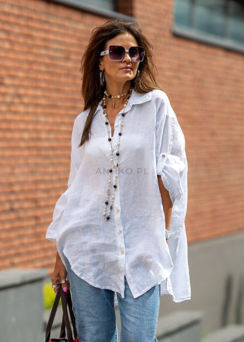 Biała lniana koszula damska oversize z asymetrycznym dołem i podpinanymi rękawami, zestawiona z jeansami w codziennej, eleganckiej stylizacji.