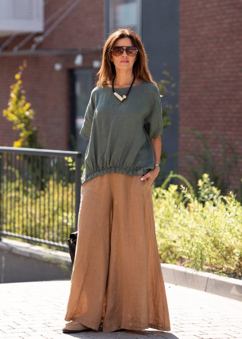 Lniana bluzka oversize w kolorze khaki ze ściągaczem u dołu, zestawiona z jasnymi spodniami w naturalnej, miejskiej stylizacji.