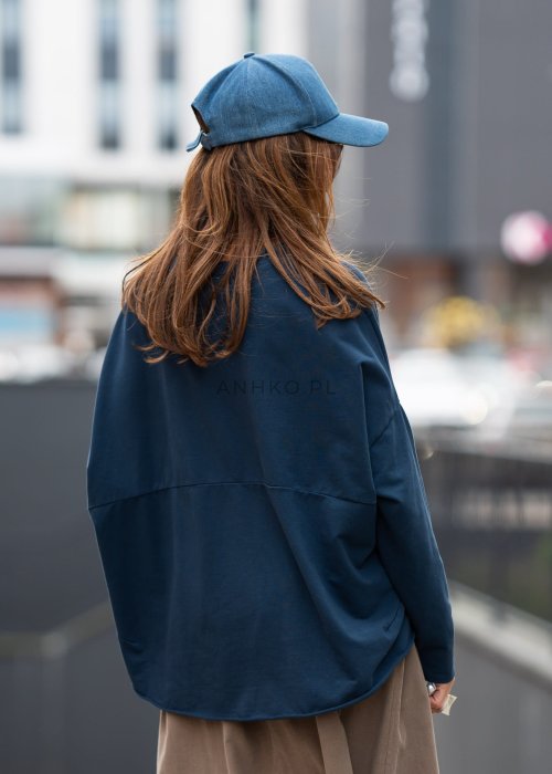 Ciemnoniebieska bluza damska oversize z długim rękawem i naszywką na froncie. Luźny fason w miejskiej stylizacji z czapką i spódnicą.