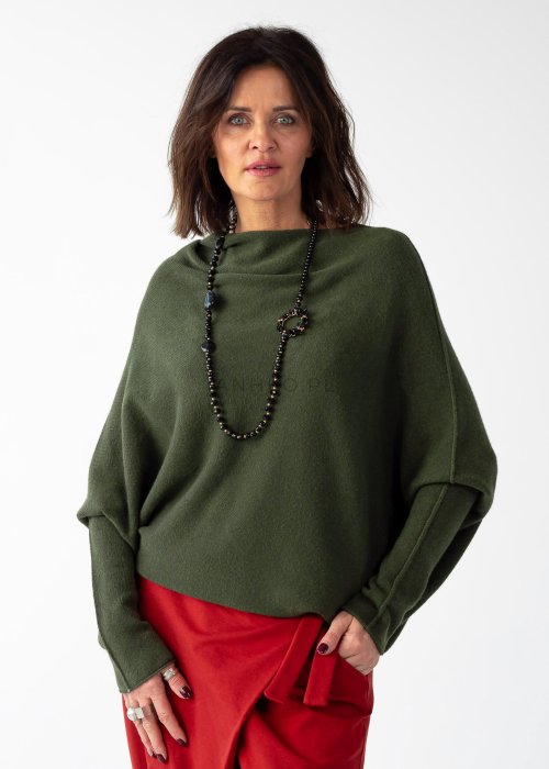 Khaki sweter oversize o nietoperzowym kroju z dekoltem łódka i asymetrycznym dołem zestawiony z czerwonymi szerokimi spodniami i długim naszyjnikiem.