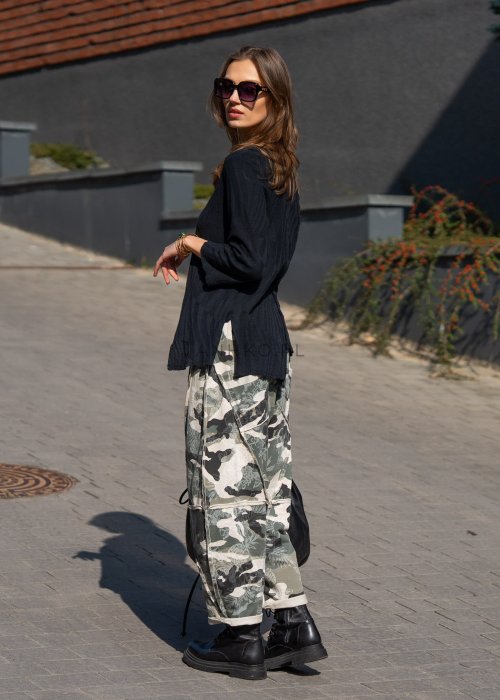 Damskie spodnie dresowe w print moro z motywem roślinnym, o luźnym kroju z kieszeniami i przeszyciami. Stylizacja z podwiniętymi nogawkami i czarnymi botkami.