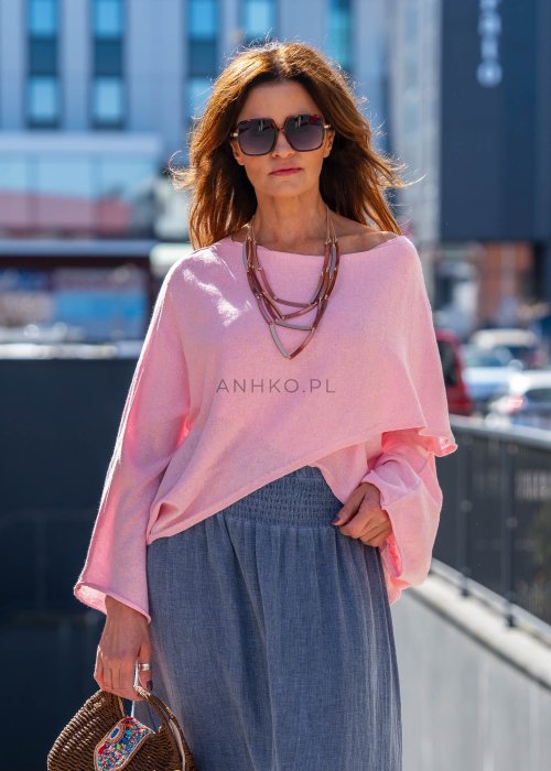 Jasnoróżowy sweter oversize z bawełnianej dzianiny i asymetrycznym dołem, zestawiony z długą szarą spódnicą w eleganckiej miejskiej stylizacji.