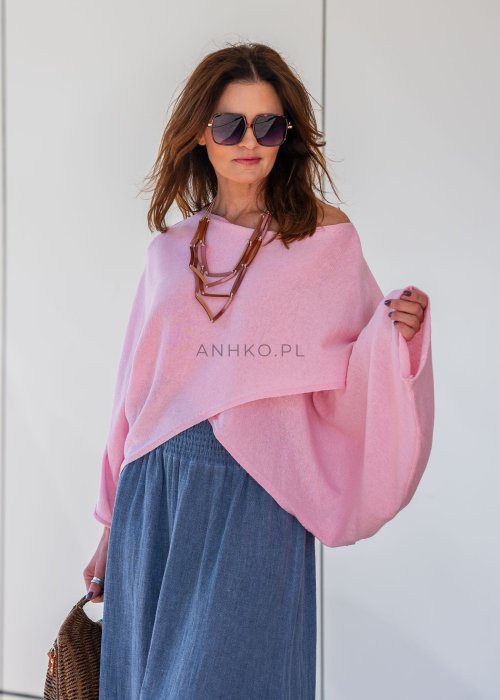 Jasnoróżowy sweter oversize z bawełnianej dzianiny i asymetrycznym dołem, zestawiony z długą szarą spódnicą w eleganckiej miejskiej stylizacji.