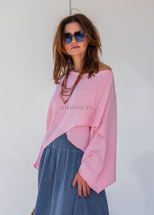 Jasnoróżowy sweter oversize z bawełnianej dzianiny i asymetrycznym dołem, zestawiony z długą szarą spódnicą w eleganckiej miejskiej stylizacji.