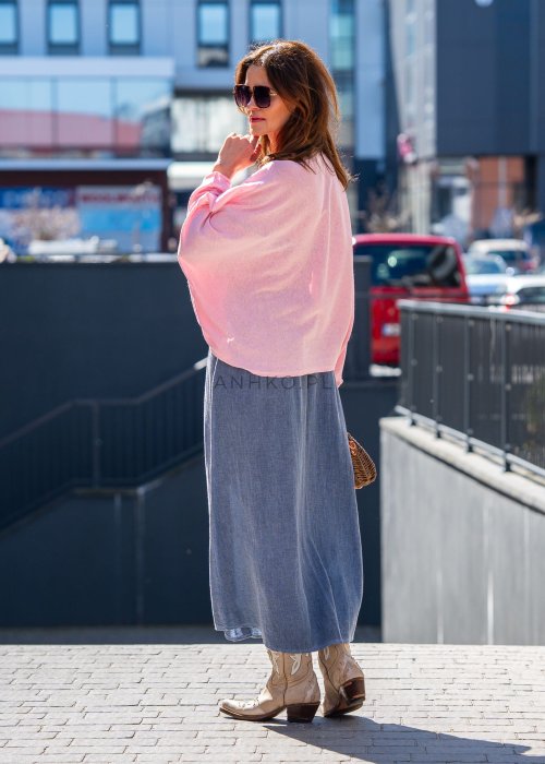 Jasnoróżowy sweter oversize z bawełnianej dzianiny i asymetrycznym dołem, zestawiony z długą szarą spódnicą w eleganckiej miejskiej stylizacji.