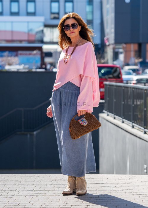 Jasnoróżowy sweter oversize z bawełnianej dzianiny i asymetrycznym dołem, zestawiony z długą szarą spódnicą w eleganckiej miejskiej stylizacji.