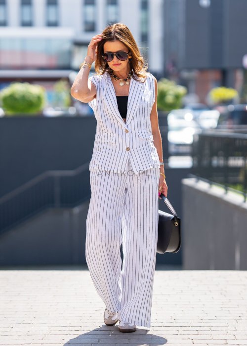 Biała kamizelka lniana damska w pionowe paski z klapami i zapięciem na dwa guziki, zestawiona z szerokimi spodniami w komplecie. Elegancka stylizacja miejska z lekką kamizelką bez rękawów.