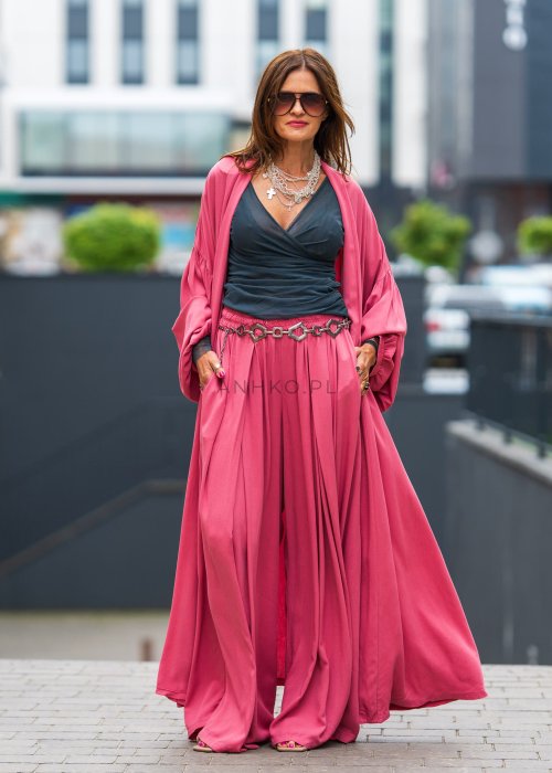 Różowe kimono damskie maxi z długim, płynnie układającym się fasonem i bufiastymi rękawami. Model pokazany w stylizacji z topem i szerokimi spodniami, w nowoczesnym miejskim wydaniu.