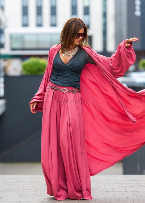 Różowe kimono damskie maxi z długim, płynnie układającym się fasonem i bufiastymi rękawami. Model pokazany w stylizacji z topem i szerokimi spodniami, w nowoczesnym miejskim wydaniu.