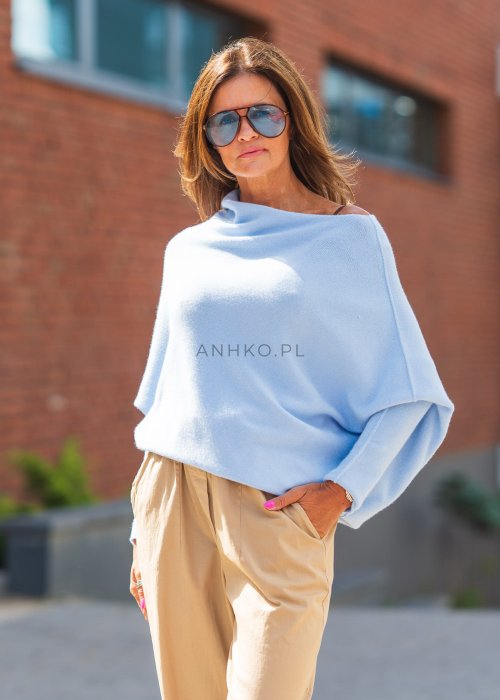 Błękitny sweter oversize o nietoperzowym kroju z dekoltem łódką i asymetrycznym dołem, stylizowany z beżowymi szerokimi spodniami.