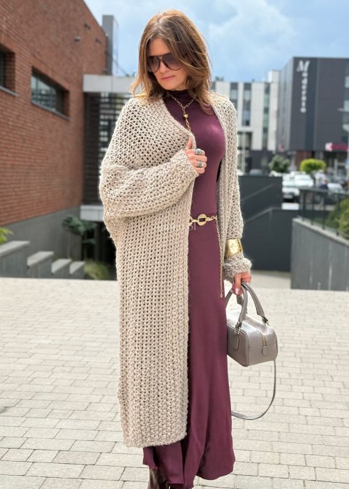 Długi oversize kardigan damski z grubego beżowego splotu, z obniżoną linią ramion, w stylu boho i casualowej mody damskiej