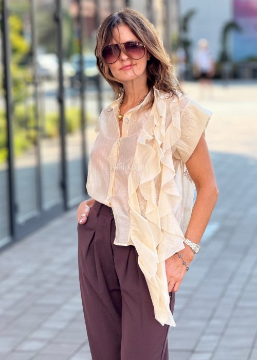 Beżowa bluzka damska bez rękawów, zapinana na guziki, z dekoracyjną falbaną z przodu, elegancki styl boho