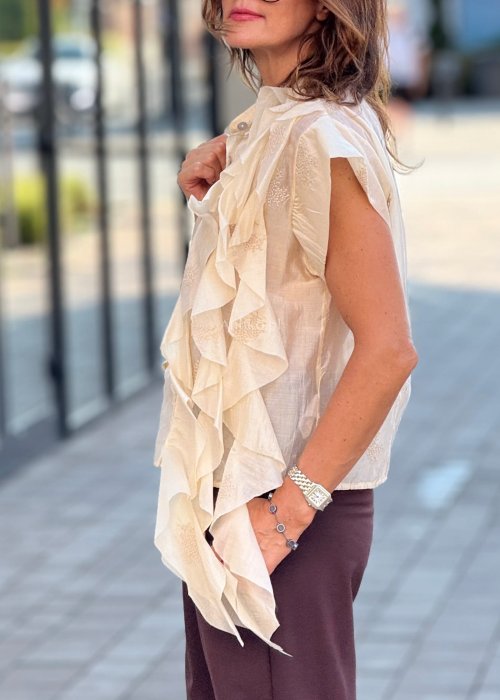 Beżowa bluzka damska bez rękawów, zapinana na guziki, z dekoracyjną falbaną z przodu, elegancki styl boho