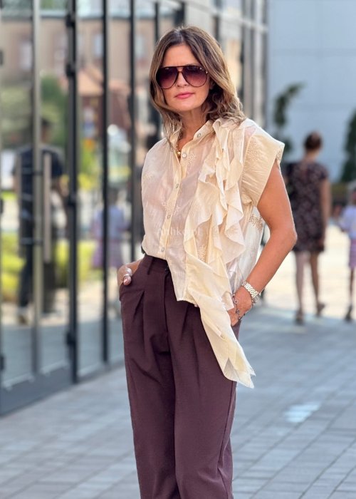 Beżowa bluzka damska bez rękawów, zapinana na guziki, z dekoracyjną falbaną z przodu, elegancki styl boho