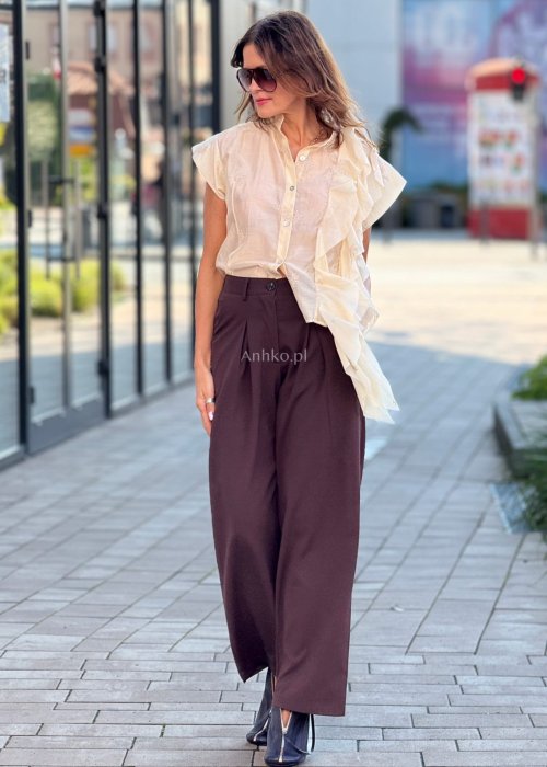 Beżowa bluzka damska bez rękawów, zapinana na guziki, z dekoracyjną falbaną z przodu, elegancki styl boho
