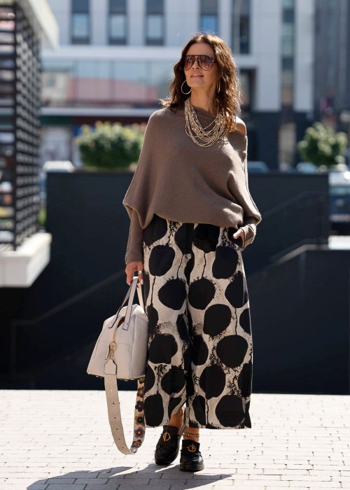 Sweter damski oversize w kolorze dark taupe o kroju nietoperzowym, noszony na jedno ramię w miejskiej stylizacji.