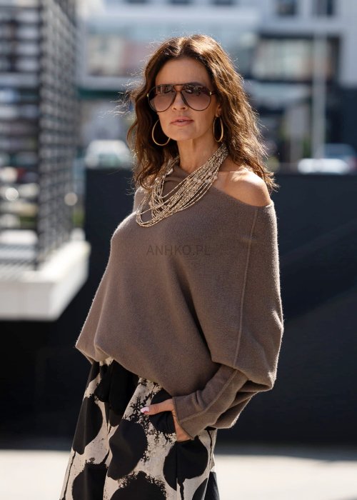 Sweter damski oversize w kolorze dark taupe o kroju nietoperzowym, noszony na jedno ramię w miejskiej stylizacji.