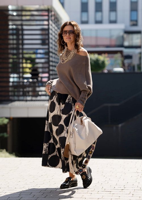 Sweter damski oversize w kolorze dark taupe o kroju nietoperzowym, noszony na jedno ramię w miejskiej stylizacji.