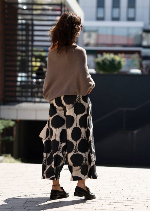 Sweter damski oversize w kolorze dark taupe o kroju nietoperzowym, noszony na jedno ramię w miejskiej stylizacji.