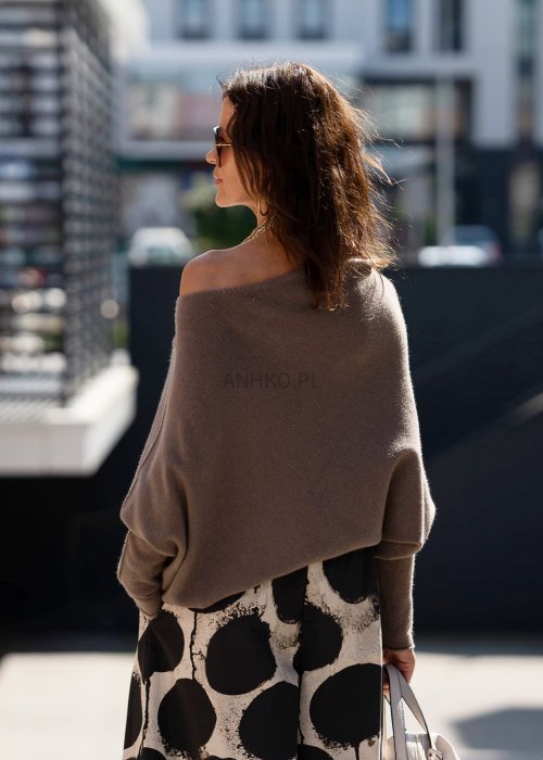 Sweter damski oversize w kolorze dark taupe o kroju nietoperzowym, noszony na jedno ramię w miejskiej stylizacji.