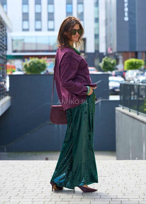 Śliwkowa bluza damska oversize z długim rękawem i okrągłym dekoltem, zestawiona z zieloną spódnicą i biżuterią w stylu miejskim.