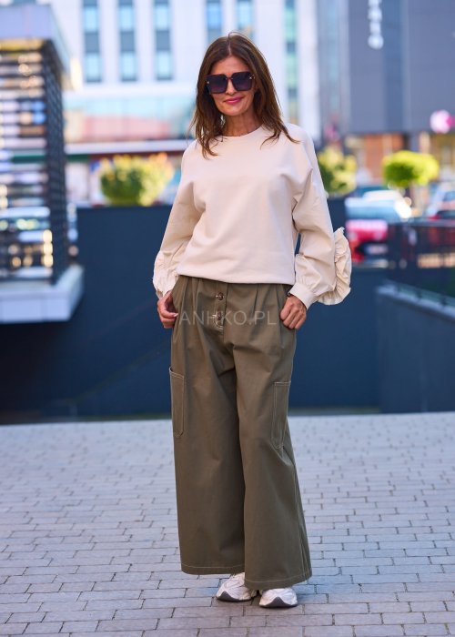 Luźne, szerokie spodnie w kolorze khaki o casualowym charakterze. Model z wysokim stanem, zapinany na duże, ozdobne guziki przesunięte lekko na bok, co nadaje im oryginalności.