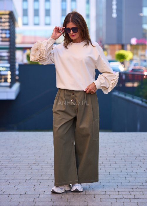 Luźne, szerokie spodnie w kolorze khaki o casualowym charakterze. Model z wysokim stanem, zapinany na duże, ozdobne guziki przesunięte lekko na bok, co nadaje im oryginalności.