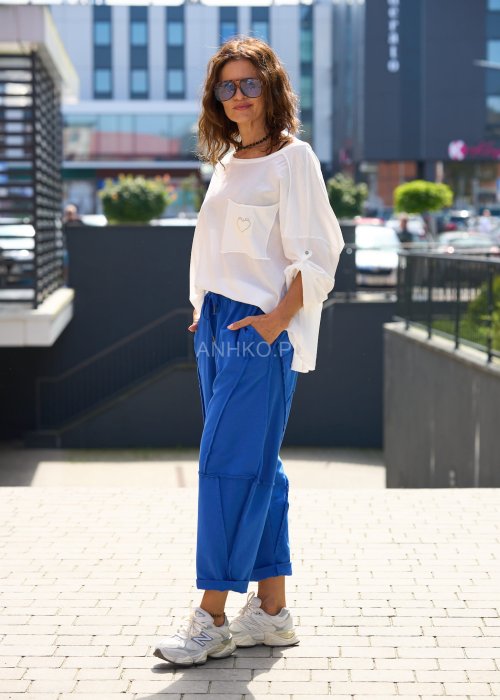 Niebieskie damskie spodnie dresowe o luźnym kroju z ozdobnymi przeszyciami i wiązaniem w pasie. Model z kieszeniami, pokazany w codziennej stylizacji ze sneakersami.