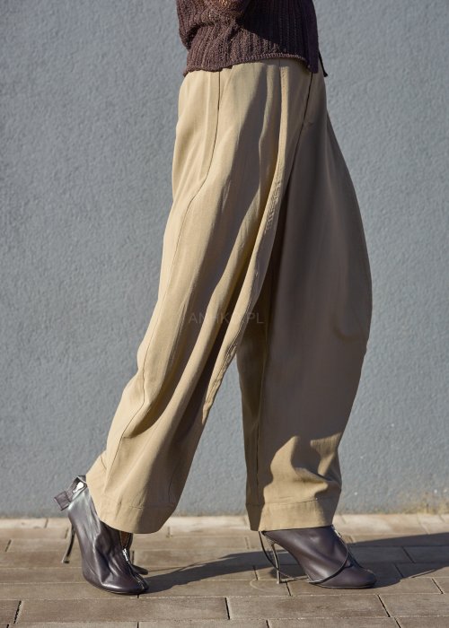 Luźne spodnie w kolorze beżowym, o szerokich nogawkach i miękkiej linii, wykonane z przewiewnego materiału, idealne do stylizacji casual i boho.