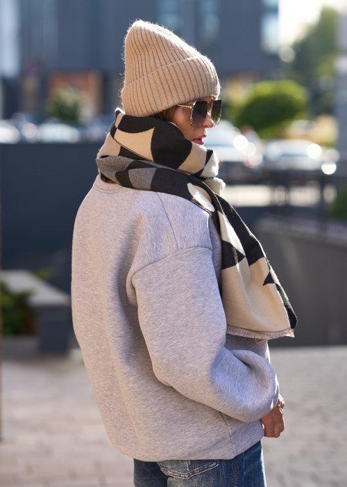 Stylizacja jesienna: beżowa czapka beanie z naszywką uśmiechu oraz duży szalik w beżowo-czarny wzór graficzny, połączone z szarą bluzą oversize i jeansami