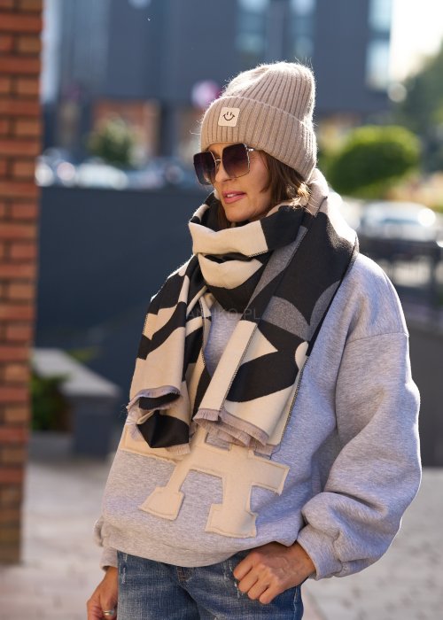 Stylizacja jesienna: beżowa czapka beanie z naszywką uśmiechu oraz duży szalik w beżowo-czarny wzór graficzny, połączone z szarą bluzą oversize i jeansami