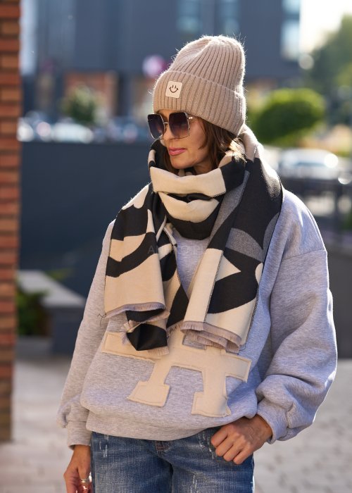 Stylizacja jesienna: beżowa czapka beanie z naszywką uśmiechu oraz duży szalik w beżowo-czarny wzór graficzny, połączone z szarą bluzą oversize i jeansami