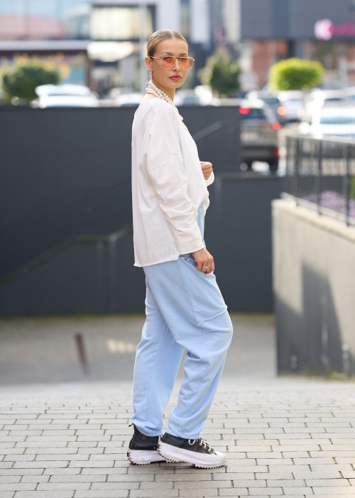 Jasnoniebieskie spodnie harem damskie z dużymi kieszeniami ozdobionymi perłami i elastyczną talią, stylizowane w miejskim looku ze sneakersami.